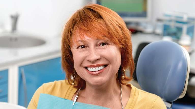 A redhead woman with white teeth sitting in a dental chair in Florida
