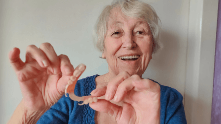 Elderly woman smiling while holding a removable partial denture.