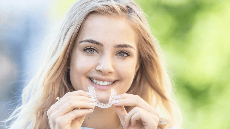 A woman smiling holding clear aligners in Lakeland, FL